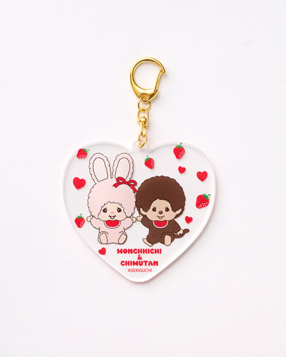 A heart-shaped acrylic keychain featuring an illustration of Monchichi and Chinuyar holding strawberries, with a gold clasp at the top, set against a plain white background.