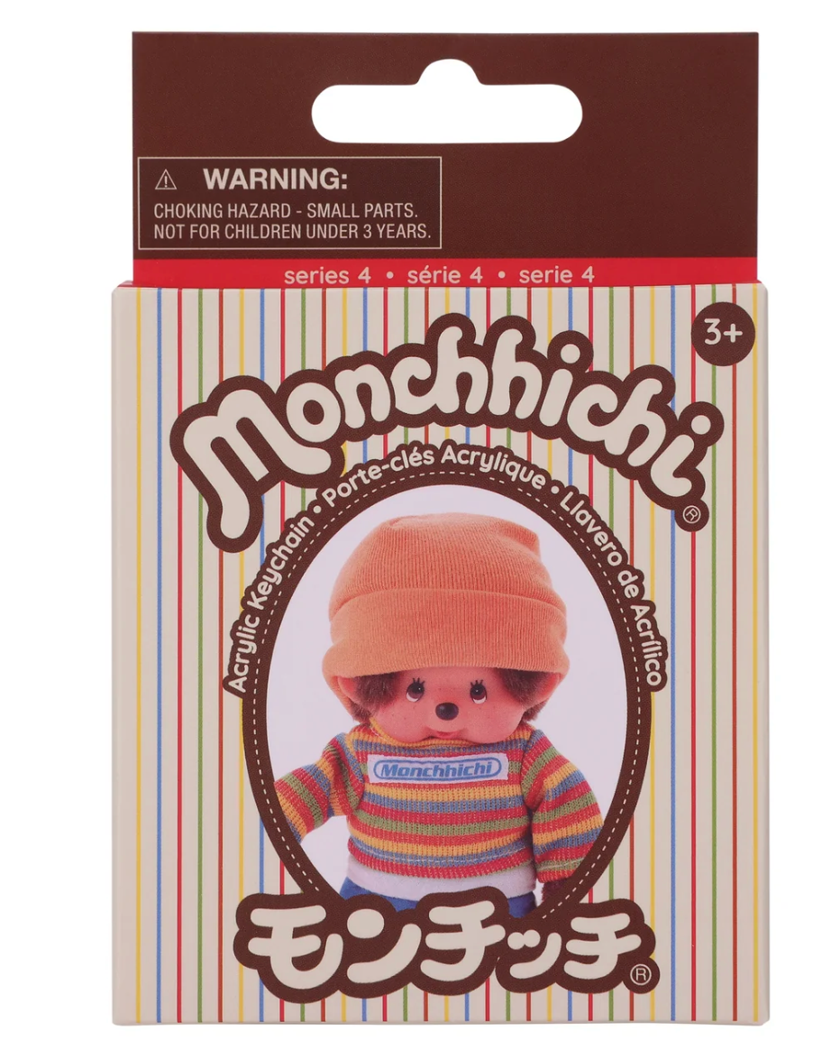 Monchhichi acrylic keychain in its original retail packaging, featuring a character wearing a peach-orange beanie and a colorful striped sweater.