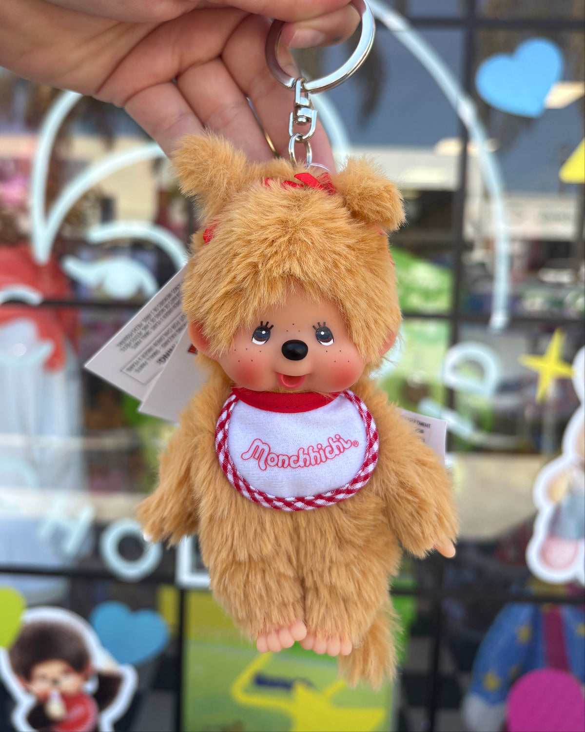 small beige monchhichi girl on a keychain in front of a store window.