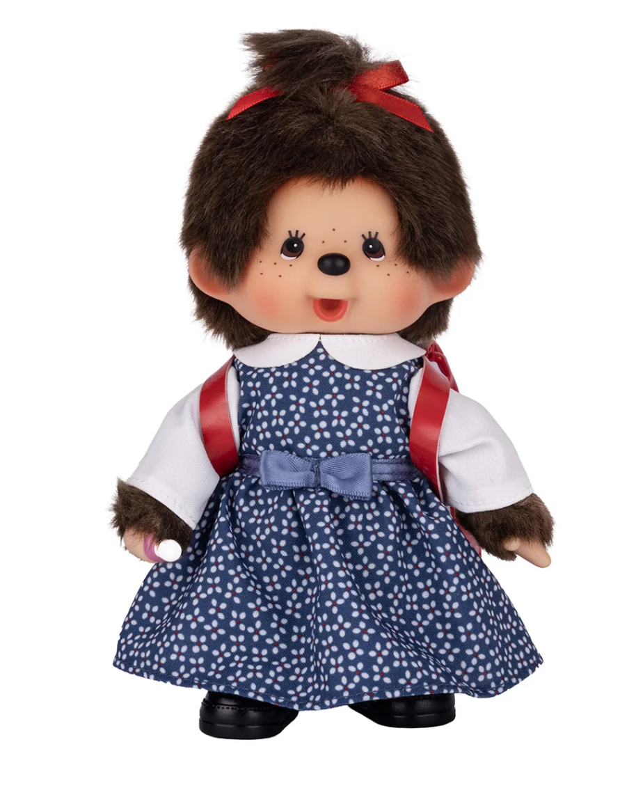 A collectible toy doll resembling a chameleon, with brown faux fur, a red bow in her hair, a navy blue polka-dot dress, a white shirt, and red suspenders, photographed against a solid white background.